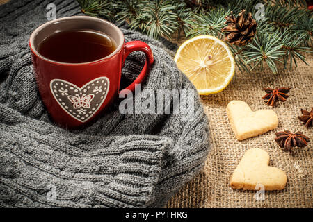 Tasse de thé rouge enveloppé dans l'écharpe de laine, tranche de citron, les branches de sapins avec cône, l'anis étoilé, cannelle et pain d'épices cookies au cœur sh Banque D'Images