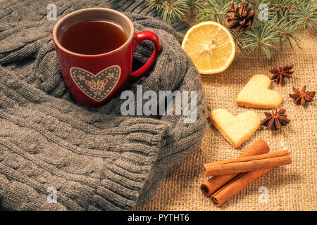 Tasse de thé rouge enveloppé dans l'écharpe de laine, tranche de citron, les branches de sapins avec cône, l'anis étoilé, cannelle et pain d'épices cookies au cœur sh Banque D'Images