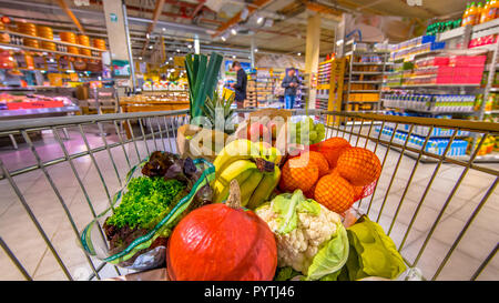 Panier d'épicerie dans un supermarché rempli de produits alimentaires frais et sain du point de l'avis des consommateurs avec des gens shopping dans backg Banque D'Images