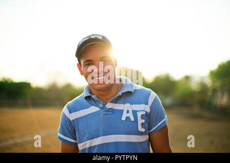 Portrait of a smiling young man standing sur un terrain de sport de l'herbe au soleil. Banque D'Images