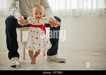 Portrait of a smiling baby girl prenant ses premiers pas assistée de son père. Banque D'Images