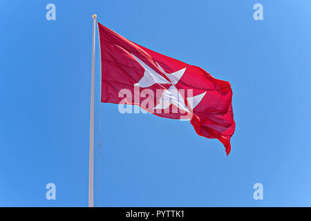 Pavillon rouge maltais avec croix blanche. Le symbole des Chevaliers de Malte est la croix à huit pointes contre le ciel bleu, l'espace de la copie Banque D'Images