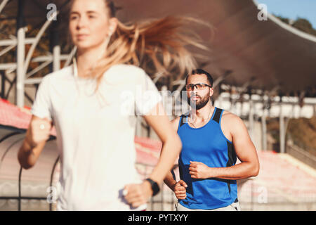 Longs cheveux blonds Sportish femme en blanc T-shirt homme barbu et multiculturelle en bleu shirt chassant l'autre à l'extérieur du stade de football, le mode de vie sain et les gens concept Banque D'Images