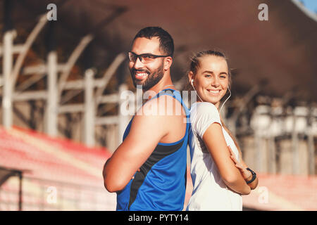 Portrait d'homme barbu beau multiculturelle en chemise bleue et sportish jolie blonde aux cheveux longs femme en blanc T-shirt debout dos à l'autre à l'extérieur du stade de football, le mode de vie sain et les gens concept Banque D'Images