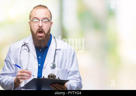Jeune médecin man holding clipboard sur fond isolé peur sous le choc avec un visage surpris, effrayé et excité avec crainte expression Banque D'Images