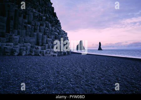 La plage de sable de lave noire et le Reynisfjara qui jouit basaltiques de Reynisdrangar sur la côte sud de l'Islande. Banque D'Images