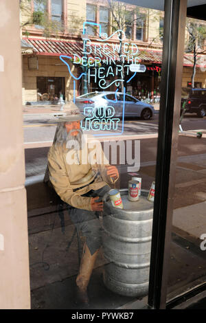 Affichage de la fenêtre dans un bar dans le centre-ville de San Antonio, Texas, USA ; prospecteur ou à l'aide d'un fût métallique de cow-boy qu'une table avec des canettes de bière sur le dessus ; Bud Light neon. Banque D'Images