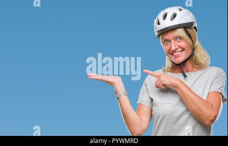 L'âge moyen caucasian woman wearing cycliste casque de sécurité au fond isolé dans l'étonnement et souriant à la caméra tout en se présentant avec la main et edition Banque D'Images