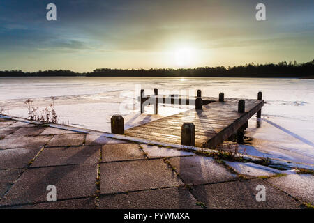 Paysage d'hiver avec le lac avec jetty couvertes de glace sous le lever du soleil de couleur ambre Banque D'Images