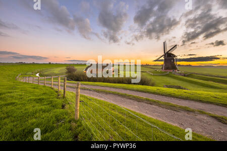 Scène ultra grand angle de moulin à vent en bois néerlandais dans le cadre du paysage herbeux plat beau coucher du soleil vu de la digue à la mer de Wadden, à Pays-Bas Banque D'Images