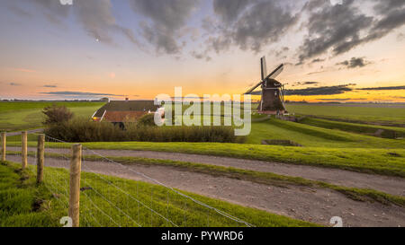 Scène ultra grand angle du néerlandais moulin à vent en bois dans les produits laitiers en paysage magnifique coucher de soleil vu de la digue à la mer de Wadden, à Pays-Bas Banque D'Images