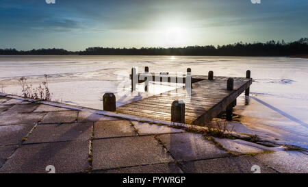 Paysage d'hiver avec lac gelé et le ponton couvert de glace sous le lever du soleil de couleur ambre Banque D'Images