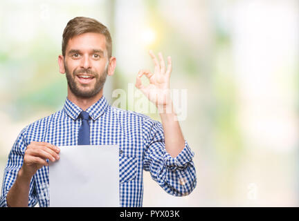 Beau Jeune homme tenant le papier blanc sur fond isolé ok faire signer avec les doigts, symbole excellent Banque D'Images