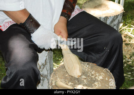 Un homme en costume national russe est à l'aide d'un couteau pour couper un morceau de bois. Banque D'Images