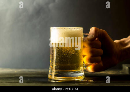 Une main tient une chope de bière fraîche. Banque D'Images