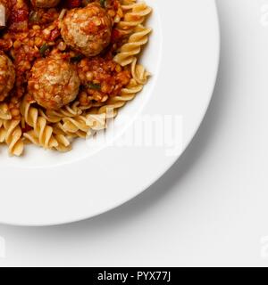 Coin d'une assiette de boulettes de viande à la tomate sause avec torsades, coller sur un fond blanc. Banque D'Images