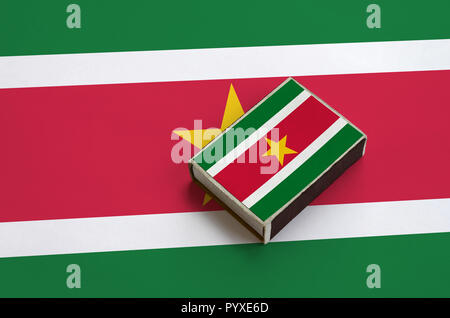 Suriname drapeau est représenté sur une boîte d'allumettes qui se trouve sur un grand drapeau. Banque D'Images