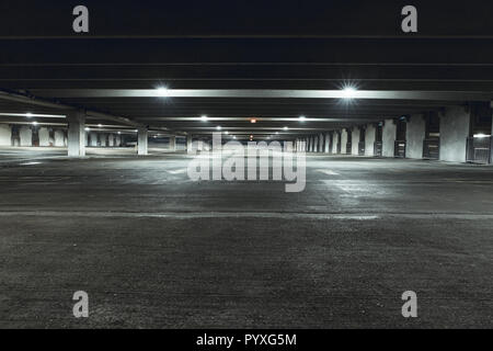Grungy, faiblement éclairées garage parking vide avec éclairage vertical et un panneau de sortie qui pendent du plafond. Banque D'Images