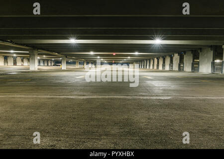 Grungy, faiblement éclairées garage parking vide avec éclairage vertical et un panneau de sortie qui pendent du plafond. Banque D'Images