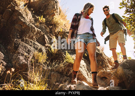 Low angle view of young man and woman walking sur une rocky mountain trail. Randonnée à travers deux terrain extrême. Banque D'Images