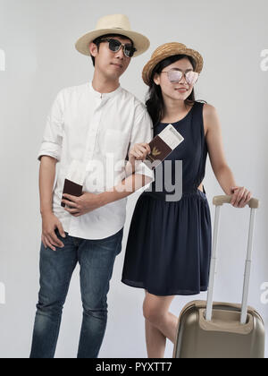 Happy Asian couple holding touristique Thaïlande passeport et valise sur fond gris. Banque D'Images