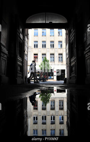 Lodz, Pologne, juillet 2018. Entrée de cour à la principale rue Piotrkowska avec une flaque d'eau et d'un immeuble et les personnes chambre reflétant en elle. Banque D'Images