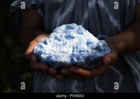 Close up of a woman holding a guérison puissante cristal de calcite bleu dans ses mains dans le noir, moody la lumière. Banque D'Images