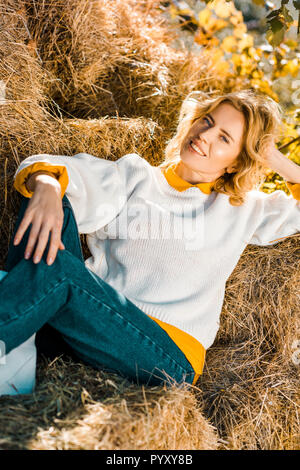 Smiling woman looking at camera et portant sur les meules de foin au ranch Banque D'Images