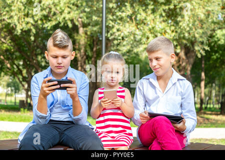 Groupe d'enfants occupés à leurs téléphones à texte sms et à l'assis à l'extérieur Banque D'Images