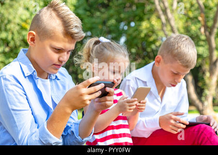 Groupe d'enfants occupés à leurs téléphones à texte sms et à l'assis à l'extérieur Banque D'Images