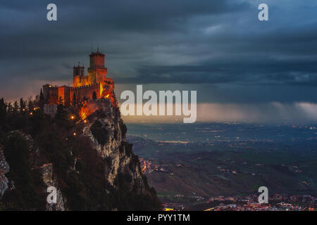 Saint-marin forteresse de Guaita sur le mont Titano au coucher du soleil. Les nuages de pluie lourde avec vue aérienne sur la ville. Location de feux de circulation et l'éclairage Banque D'Images