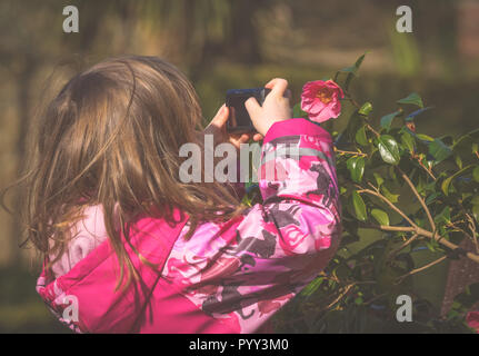 Cute little caucasian girl faire des photos de fleurs dans le parc au printemps Banque D'Images