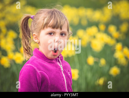 Portrait d'une jeune fille espiègle faisant étrange visage avec l'arrière-plan de jardin printemps jonquilles jaune Banque D'Images