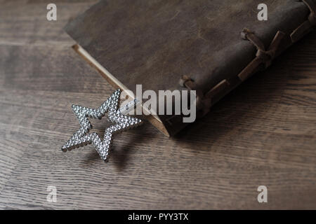 Vue en perspective du livre fermé avec cuir vintage brown contraignante et une étoile d'argent Magic wand jouet en bois brun foncé sur l'intérieur parquet backgrou Banque D'Images