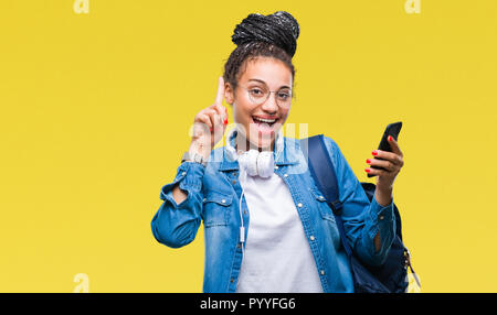 Les jeunes cheveux tressés african american girl étudiant à l'aide de blackberry sur fond isolé surpris avec une idée ou une question doigt avec hap Banque D'Images