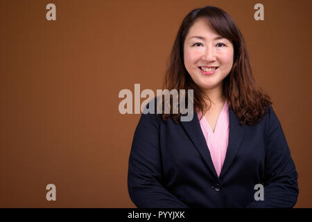 Belle mature Asian businesswoman contre fond brun Banque D'Images