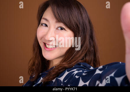 Belle mature Asian businesswoman contre fond brun Banque D'Images