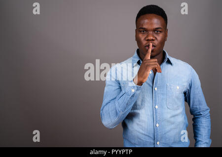 Young African man wearing denim shirt contre l'arrière-plan gris Banque D'Images