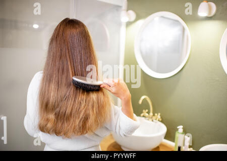 Femme en peignoir peigner les cheveux avec la brosse dans la salle de bains, vue arrière Banque D'Images