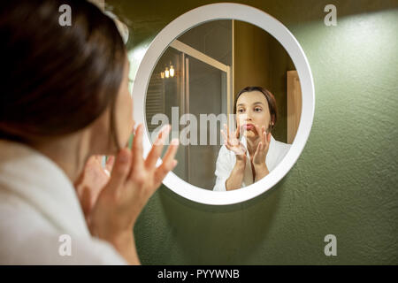 Femme en peignoir faire massage du visage à la ronde dans le miroir dans la salle de bains Banque D'Images