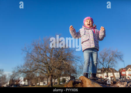 Cute little girl crier de joie en se tenant sur le haut d'un grand arbre log dans le parc au printemps Banque D'Images