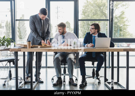 Heureux les jeunes travailleurs de bureau dans l'usure formelle eating pizza sur le lieu de travail Banque D'Images