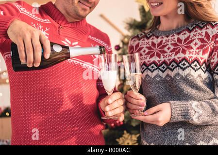 Portrait de couple dans des pulls de noël, mari pouring champagne pour femme Banque D'Images