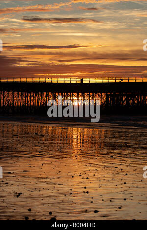 Jetée en bois d'ossature se reflétant dans les sables humides à la plage pendant le coucher du soleil Banque D'Images