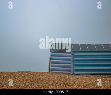 La rayé bleu et blanc cabanes de plage dans la brume sur une plage de galets Banque D'Images