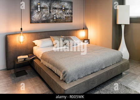 Vue d'un lit double avec draps gris à l'intérieur confortable avec des lumières, un design moderne lampe de plancher et de l'abrégé photo sur le mur Banque D'Images