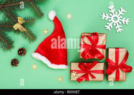 Décoration de Noël. Santa's hat, coffrets cadeaux, branches de sapins avec les cônes et décoratives snowflackes sur fond vert. Vue d'en haut. Greeti de Noël Banque D'Images