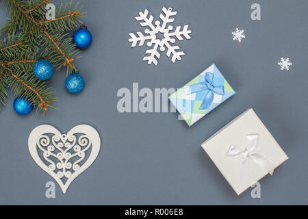 Décoration de Noël. Des boîtes-cadeaux, branches de sapins avec des boules de décoration, jouet snowflackes et coeur sur fond gris. Vue d'en haut. Vœux de Noël Banque D'Images