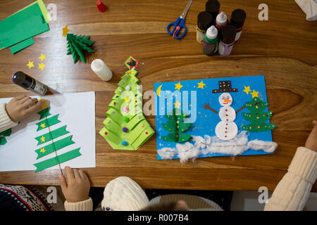 Vue de dessus de l'enfant, faisant et bonhomme hiver arbre. Bâton de colle, ciseaux, crayon, marqueurs, feuilles de papier et bouts sur fond de bois. Amusant pour les enfants wifi Banque D'Images