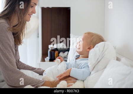 La mère et le bébé en pyjama, tôt le matin, maman prendre soin de son bébé garçon malade. Bébé au lit avec fièvre et écoulement nasal Banque D'Images